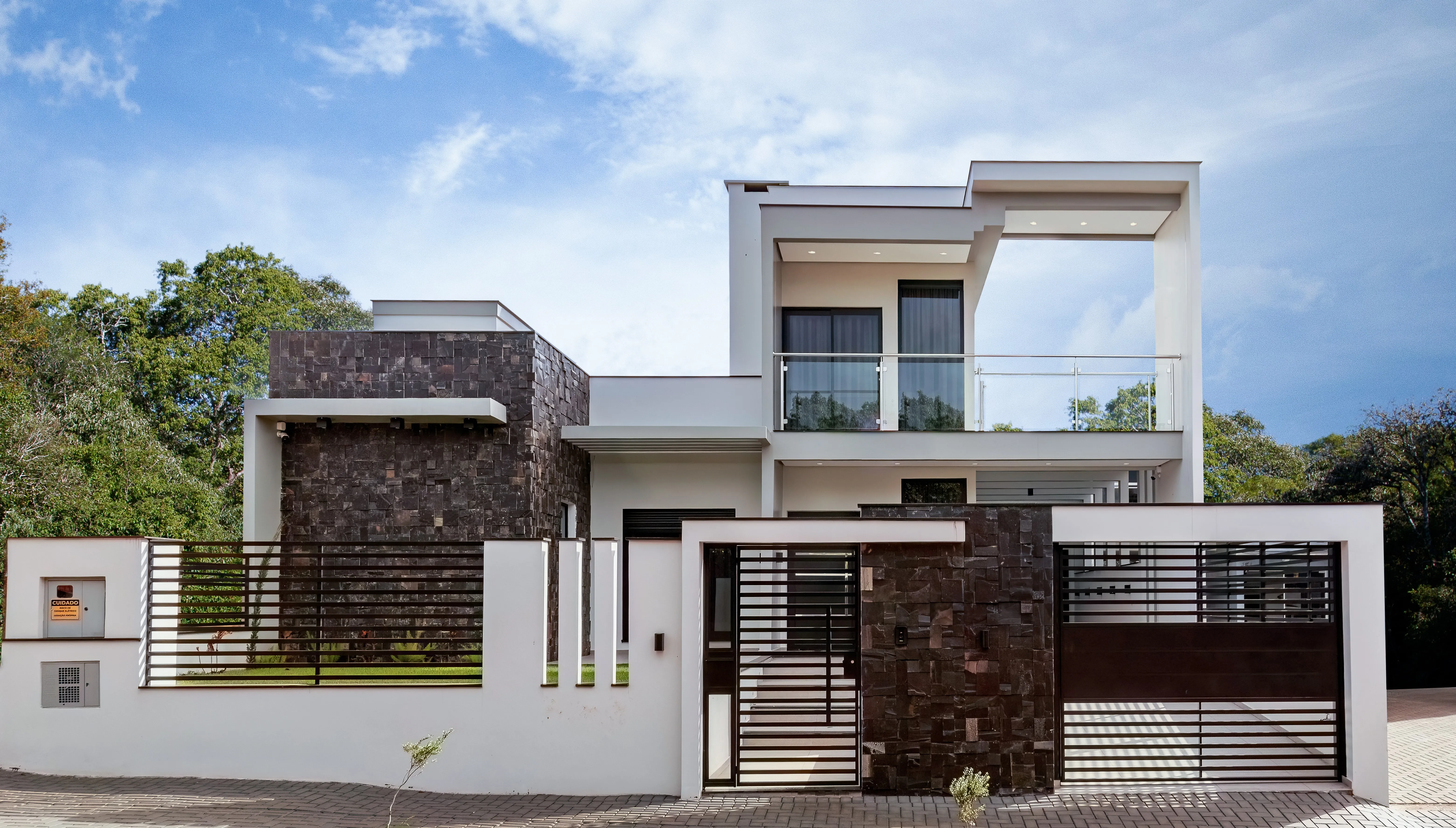 Fachada de uma residência moderna com elementos em pedra escura, grandes janelas de vidro e portão de entrada com design contemporâneo.