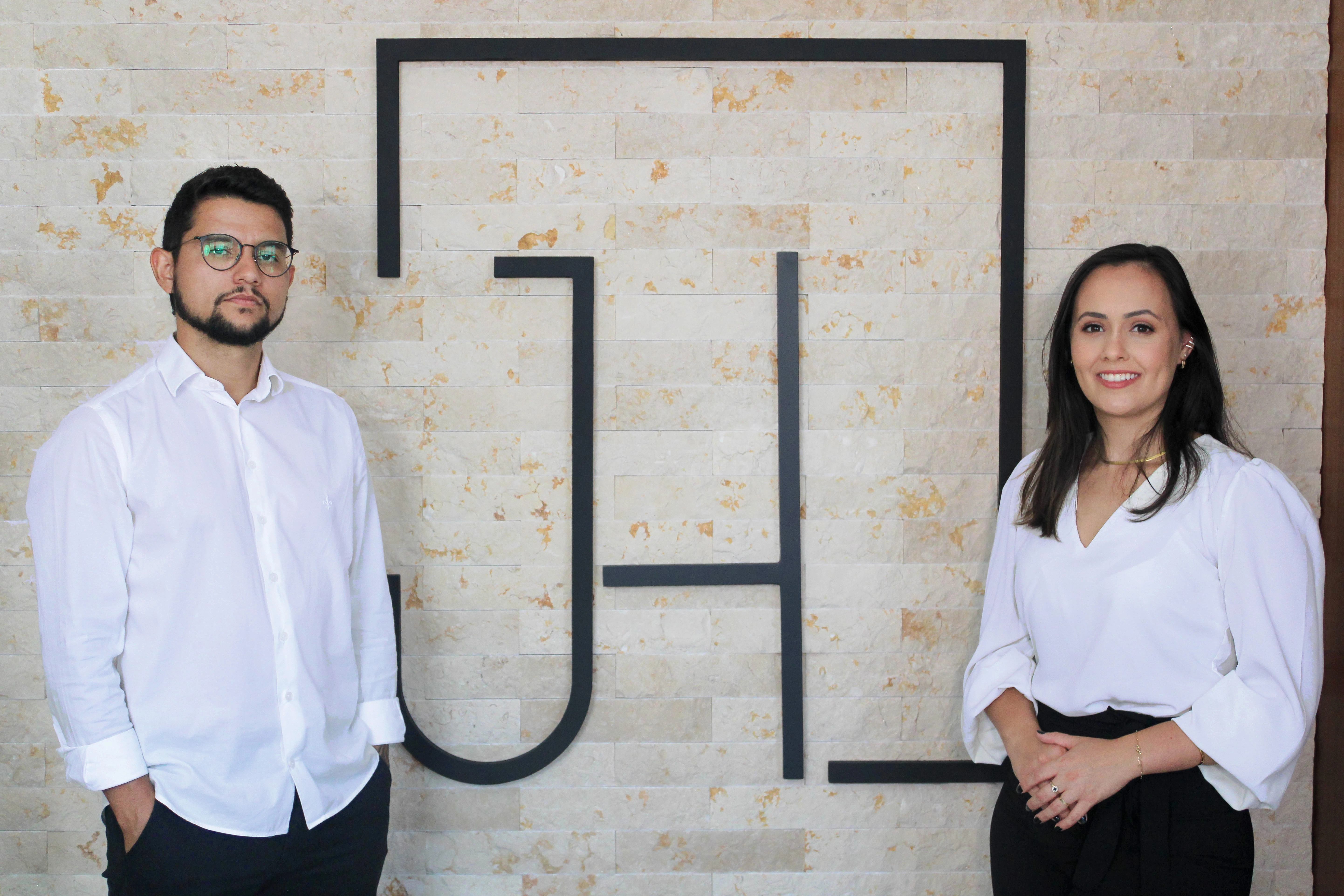 Sócios da empresa sorrindo e posando ao lado do símbolo da empresa em um ambiente corporativo.